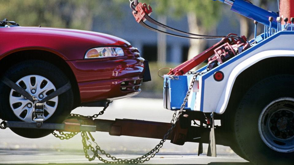 Get a load of this: a sharp close-up shot shows our reliable DFW Towing Service in action! Picture a sleek red car hooked up and ready to ride, flagged down by our blue and white tow truck, proudly displaying the "DFW Towing Service" name. The car's locked in tight with heavy-duty chains as the hydraulic arm lifts those front wheels right off the pavement. In the background, trees and buildings zoom by in a blur—because when you’re in need, we move fast!