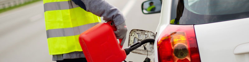 Y'all listen up! Picture this: One of our top-notch roadside heroes, decked out in a reflective yellow vest, is right there helping folks in need. He’s topping off a white car on the shoulder of the road with some good ol' reliable gasoline from a bright red can. The car's fuel cap is thrown open, and you can see that rear brake light shining clear as day. Now that's what we call first-class service here at Dallas Towing!